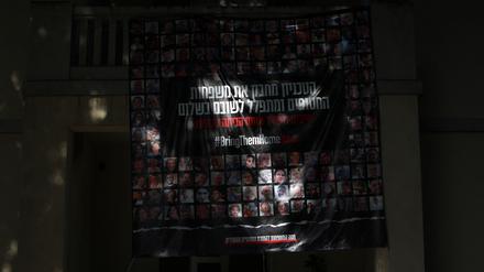 Aus dem Dunkel leuchtet ein großes Plakat mit den Gesichtern der israelischen Geiseln an einer Hauswand in Tel Aviv.