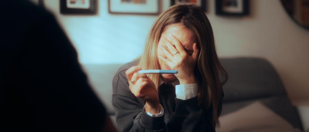 Verzweifelte Frau mit Schwangerschaftstest.
