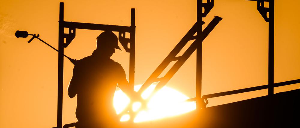 Ein Bauarbeiter steht mit einem Gasbrenner beim Bau eines Mehrfamilienhauses im Neubaugebiet Kronsrode, als am Horizont die Sonne aufgeht.  